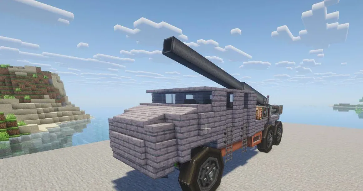 Un camion militaire en blocs, armé d’un long canon, garé sur une plage au bord de l’eau.
